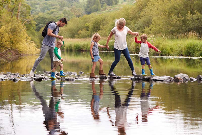 Image of a young family trying to cross a shallow river in stepping stones.