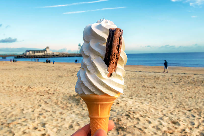 Image of a person holding an ice cream cone on the beach.