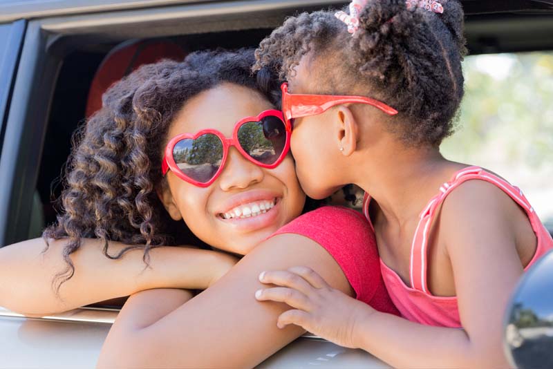Image of two children leaning out of a car window with sunglasses on.