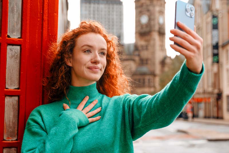 Image of a young woman taking a selfie outside a London telephone box.
